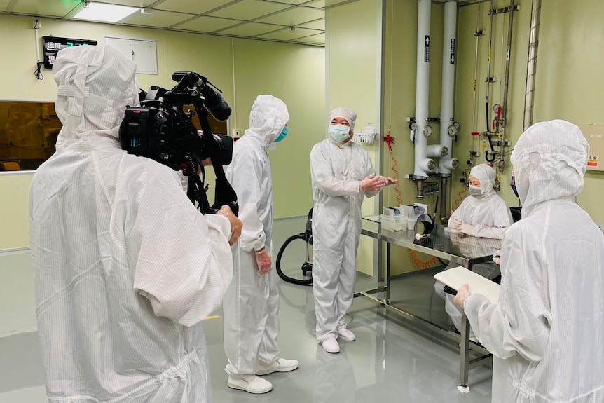 Five people wearing white overalls, masks and headwear in a science lab.