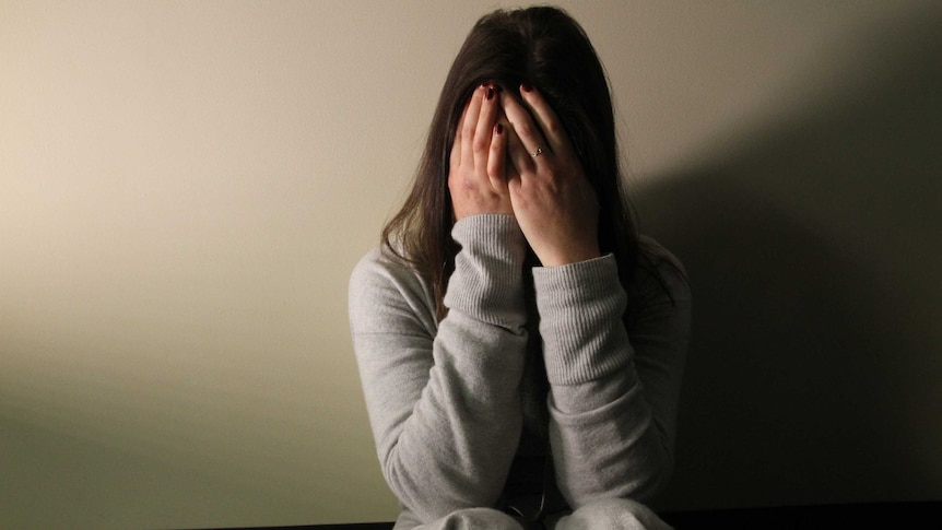 A woman covering her face and sitting on the floor upset