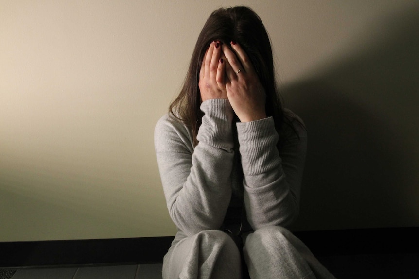 A woman covering her face and sitting on the floor upset