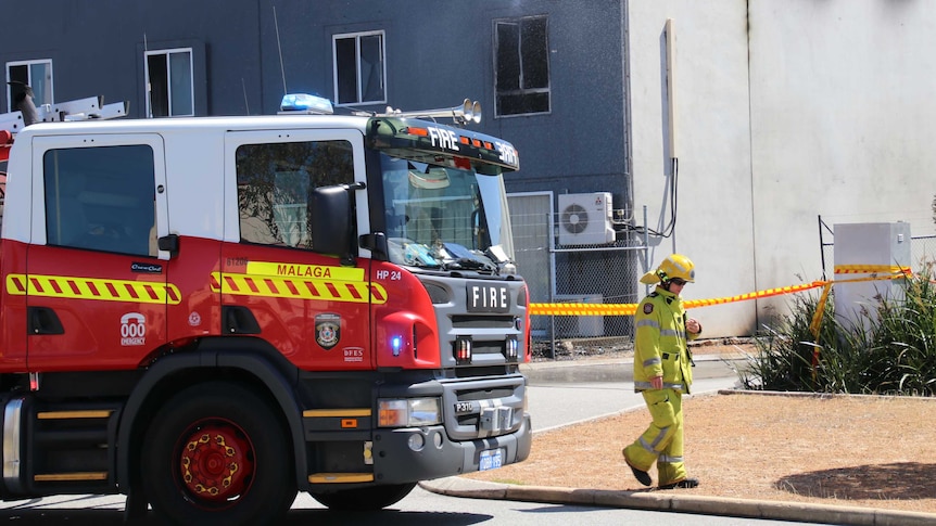 A firefighter walks in front of a truck, in front of the building.