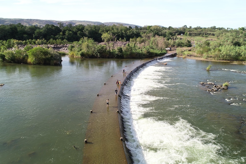 people fish off a flowing causeway spanning a river