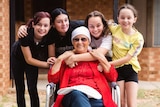 A woman wearing a head scarf sits in a folding chair surrounded by four girls.
