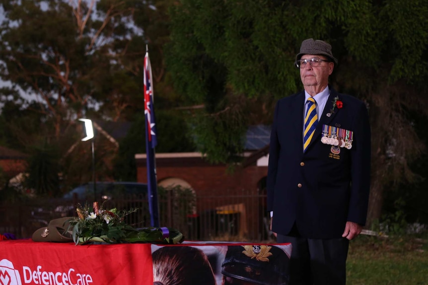 a man in uniform wearing medals stands next to the Australian flag