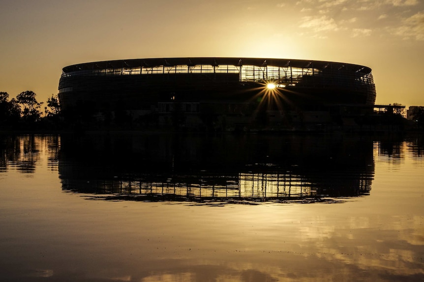 Perth Stadium in silhouette at sunrise.