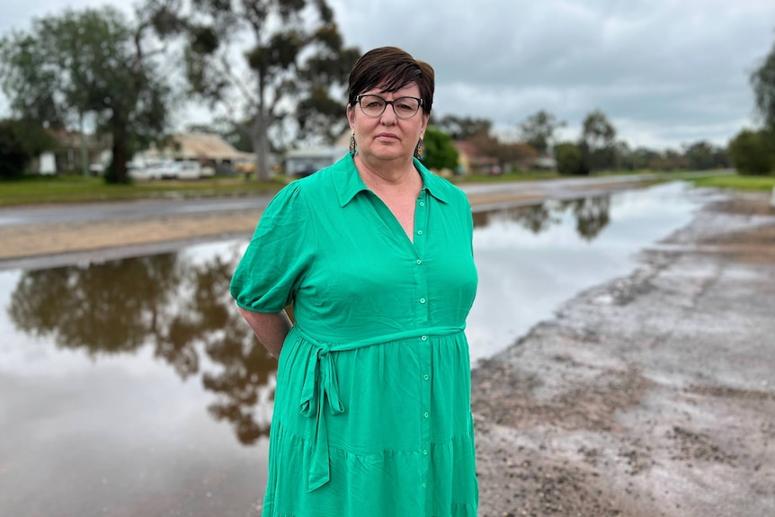A woman in a green dress stands in front of a flooded road