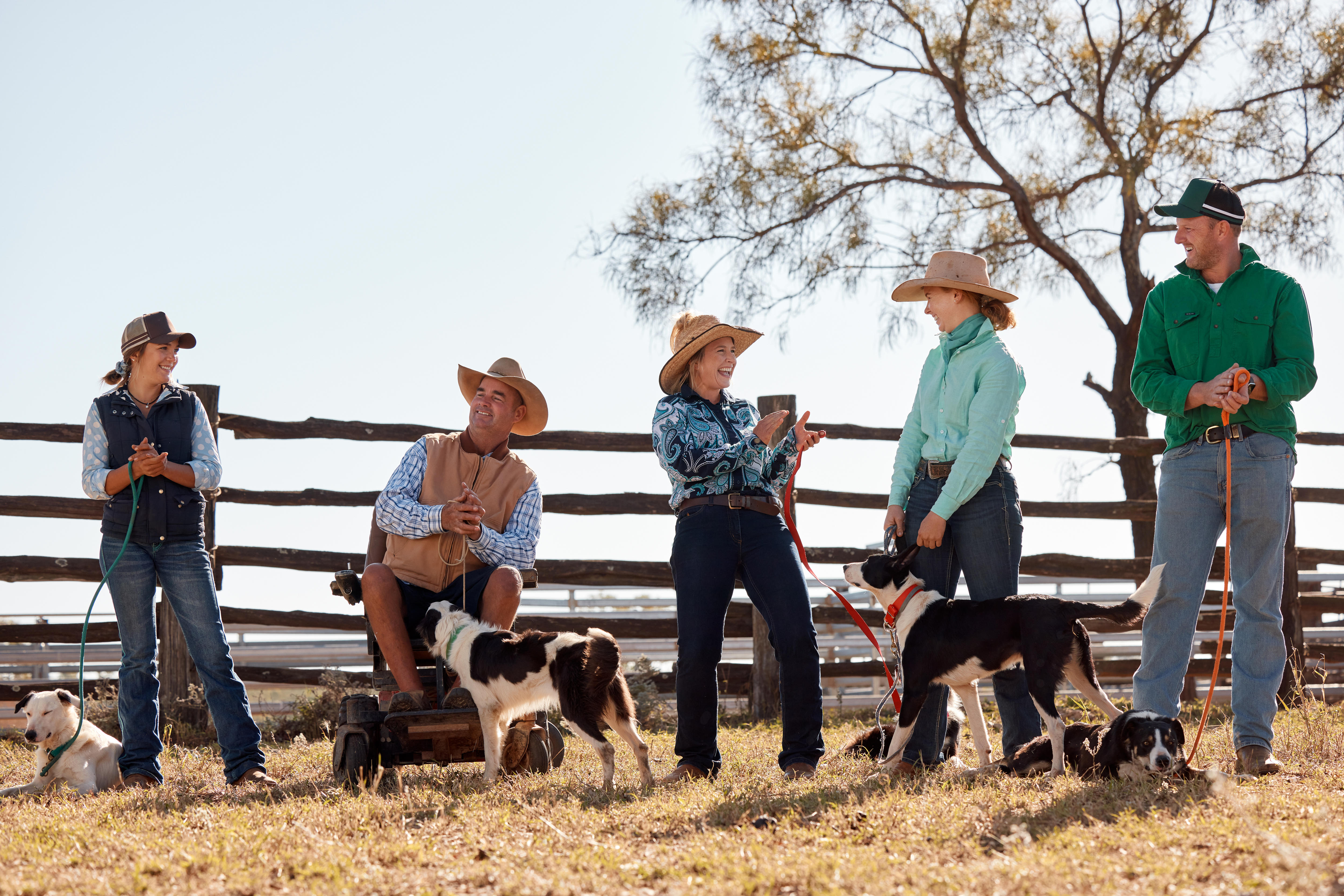 A group of smiling people in farm gear stand near a fence.