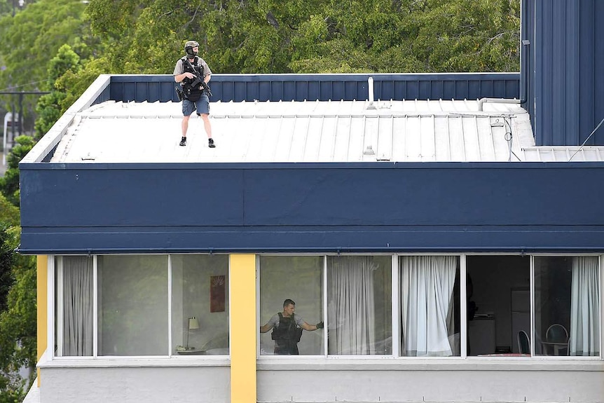 An armed policeman on the roof of a building and another officer at the window of a top-floor apartment