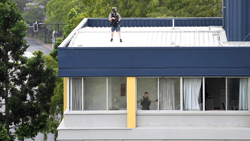 An armed policeman on the roof of a building and another officer at the window of a top-floor apartment