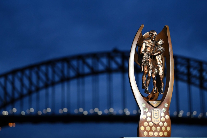 The NRL premiership Provan-Summons trophy sits in front of the Sydney Harbour Bridge at night.
