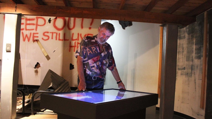 A man stands above a glowing touch screen installation at a museum.