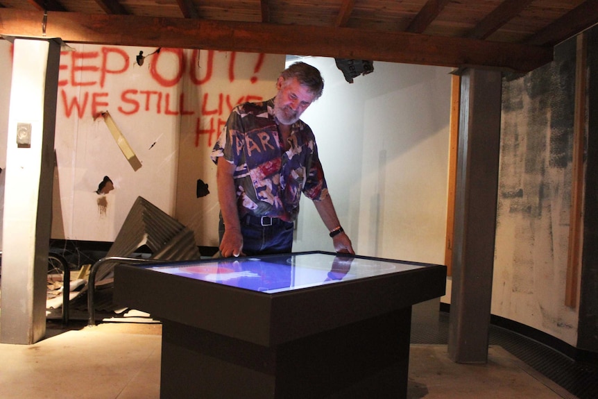 A man stands above a glowing touch screen installation at a museum.