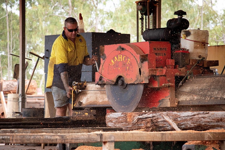 A man in a high vis shirt operate a large saw on planks of timber