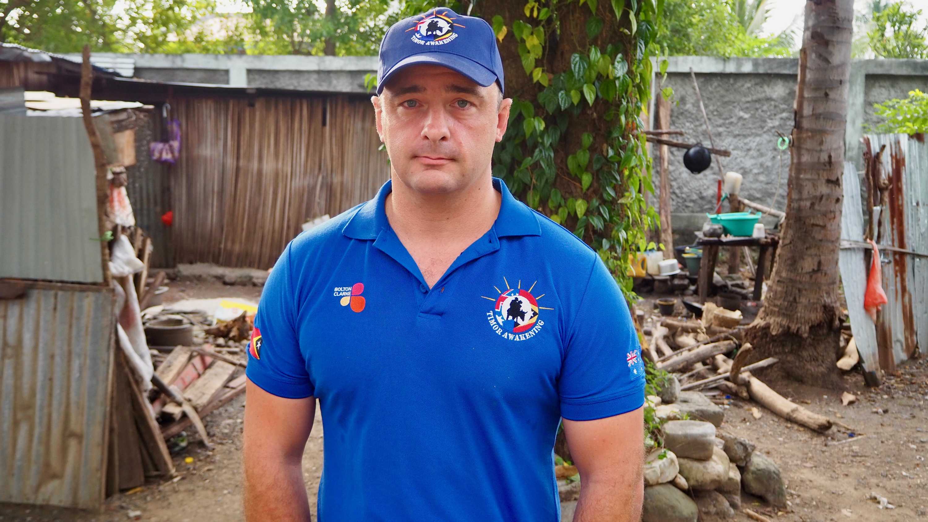 A man in a blue shirt and matching cap is standing outside