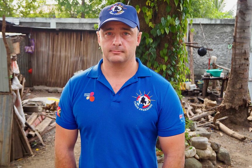 A man in a blue shirt and matching cap is standing outside