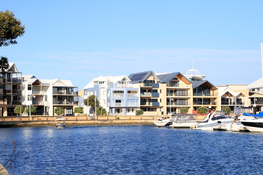 Multi-storey houses line a stretch of water with pleasure boats in the right foreground.