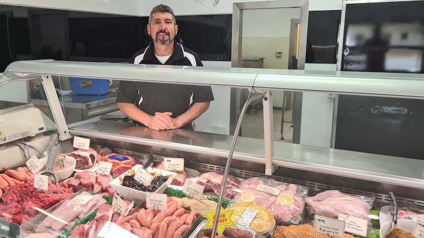 Midde-aged man standing in front of counter full of meat 