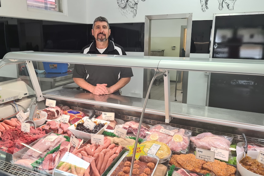 Midde-aged man standing in front of counter full of meat 