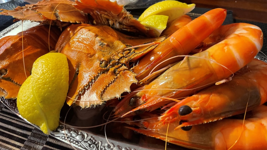 A silver platter full of wild-caught prawns and Balmain bugs served with lemon wedges.