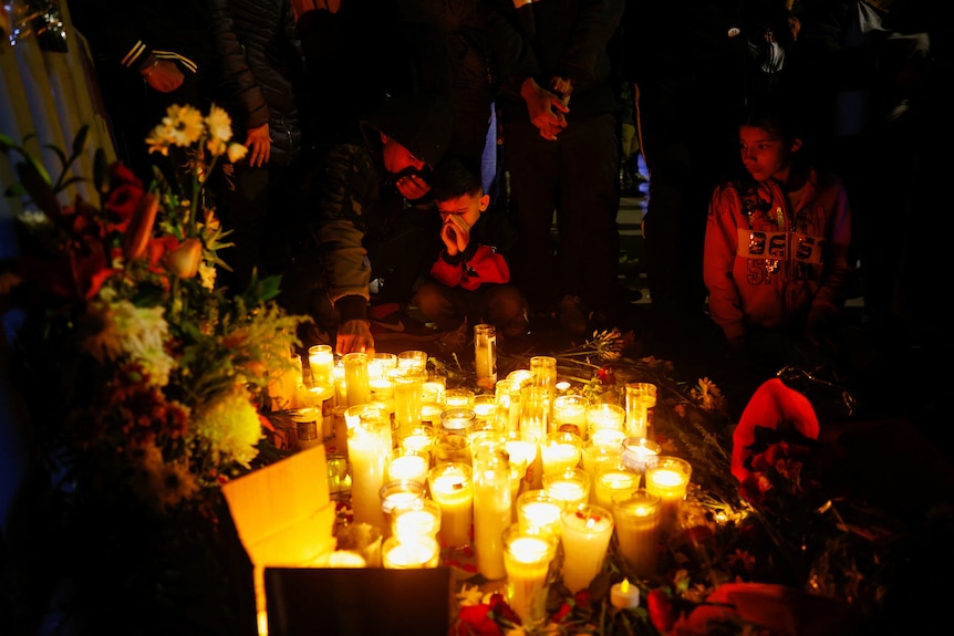People lit by candlelight in front of flowers and candles at night-time vigil.