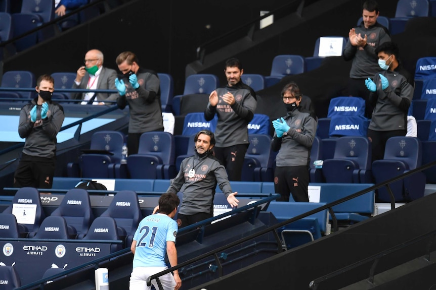 A Premier League player runs up the steps after a match as club workers applaud in the stands.