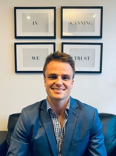 A man in suit sits in front of a wall with four framed pictures