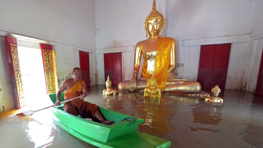 A Buddhist monk paddles past a statue of Buddha in floodwaters.