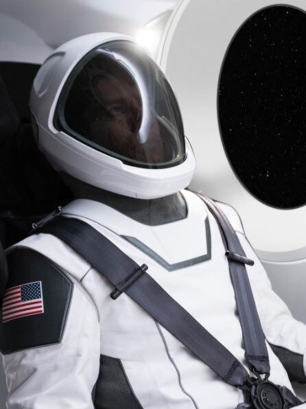 A man in a black and white spacesuit with the American flag on the arm, strapped into a spacecraft.