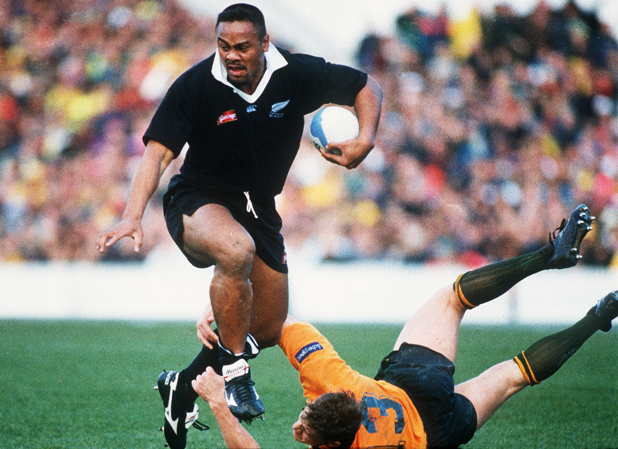 Jonah Lomu corre com a bola enquanto um oponente dos Wallabies não consegue fazer um tackle durante uma partida de teste de 1995.