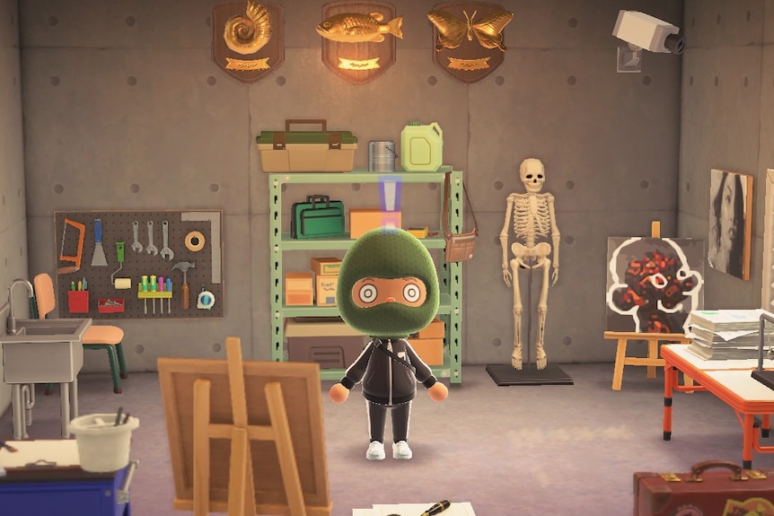 A 3D game character wears green balaclava, black jumpsuit and stands in concrete room with art tools, supplies and canvases.