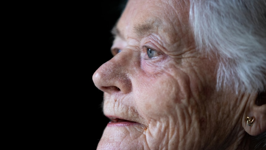 An older woman looks out a window with a content expression.