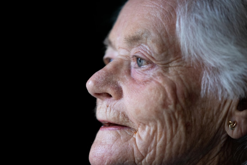 An older woman looks out a window with a content expression.