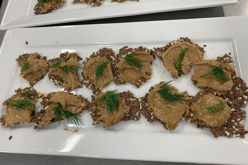 Photo of pate on handmade crackers. They are topped with sprigs of dill and are set out on a white, oblong china platter.