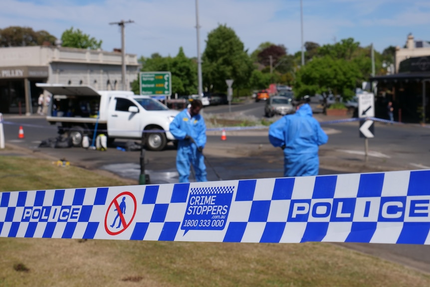 police tape with cleaners wearing blue protective clothing, roundabout in background