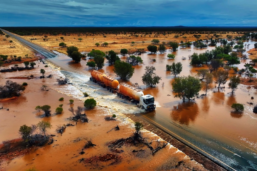 A drone shot of a road train crossing a flooded road.