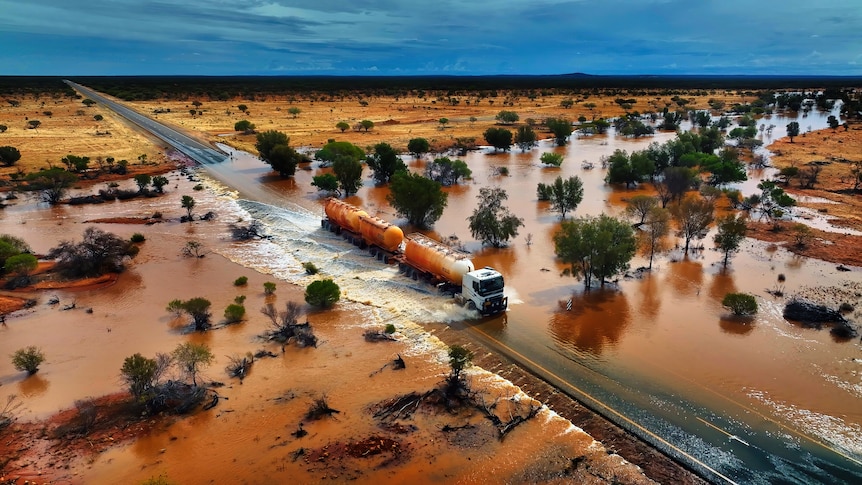 A drone shot of a road train crossing a flooded road.