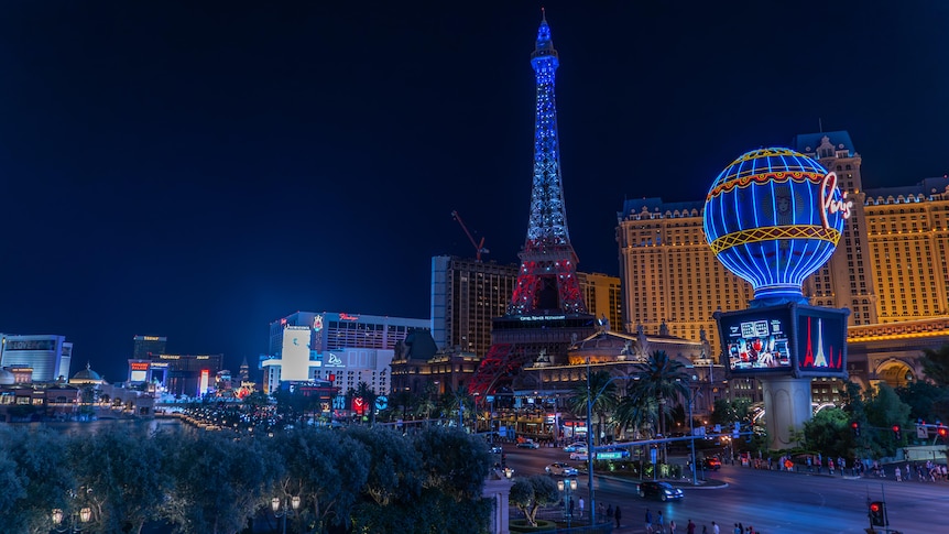 The Las Vegas strip at night, including a replica Eiffel Tower and large hotel, lit up in bright colours.