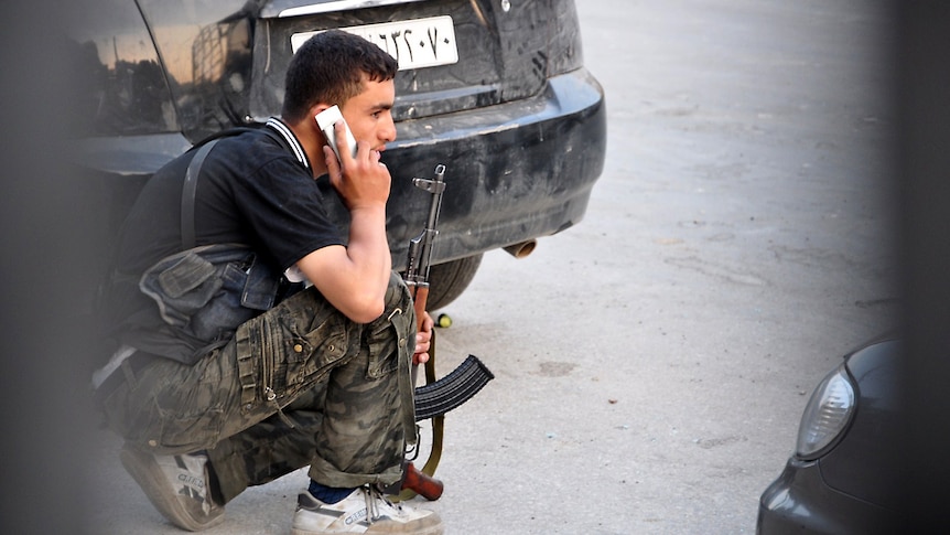 A Syrian rebel talks on the phone as he takes position during clashes with government troops at a police station in Aleppo.