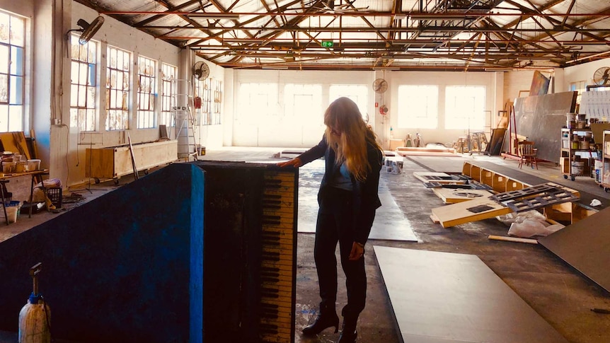Emma Kingsbury inspects a fake grand piano propped up on its side in a light-filled workshop space.