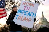 Christina Young holds a "Honk to Impeach Trump" sign outside of Longworth House Office Building