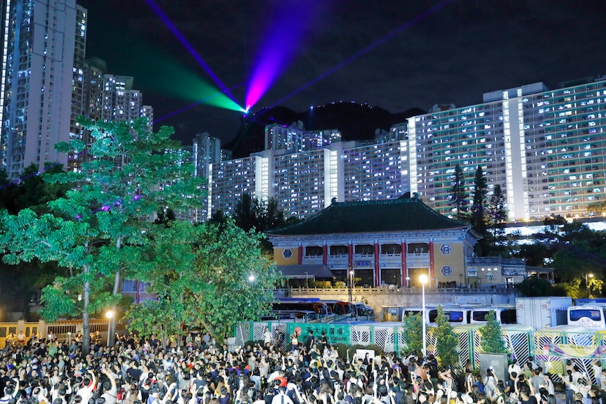 Looking up to Hong Kong's Lion Rock, you view a line of lazers and smartphone lines line its peak as a large crowd looks on.