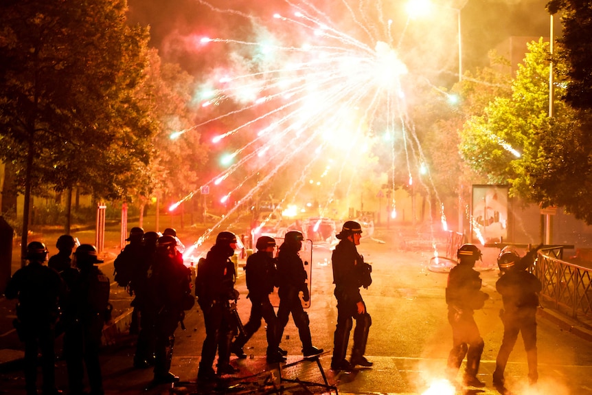 French police stand in position as fireworks go off during clashes with youth.