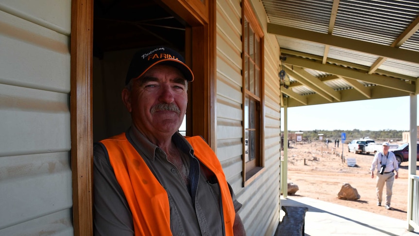 A man with a grey moustache wearing an orange work vest stands against a doorframe of Patterson House.
