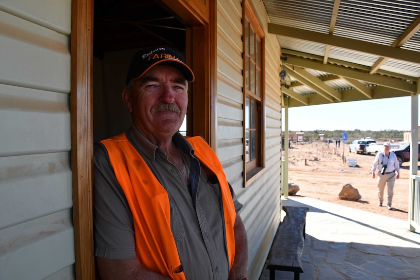 A man with a grey moustache wearing an orange work vest stands against a doorframe of Patterson House.