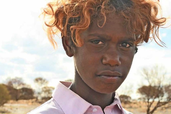 Young indigenous man with disheveled orange hair wearing a pink shirt and looking at the camera