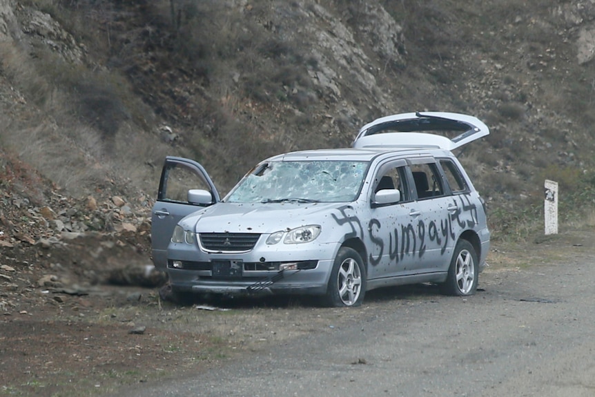 You view a silver wagon with swastika graffiti sprayed onto it, while a blurred image of a corpse appears behind the vehicle.