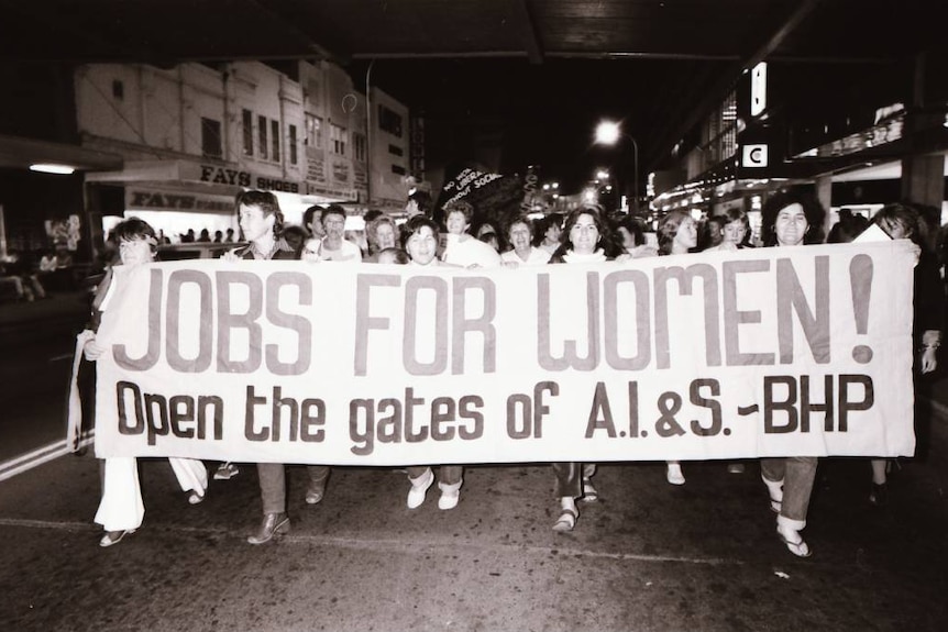 Black and white photo of women marching with a banner reading 'Jobs for Women!'