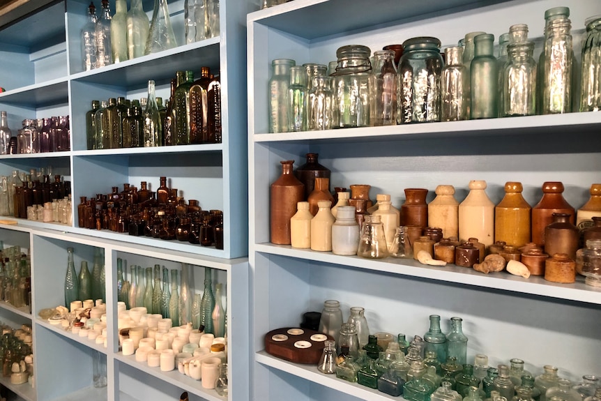 A large collection of coloured glass bottles and other artefacts arranged on shelves.