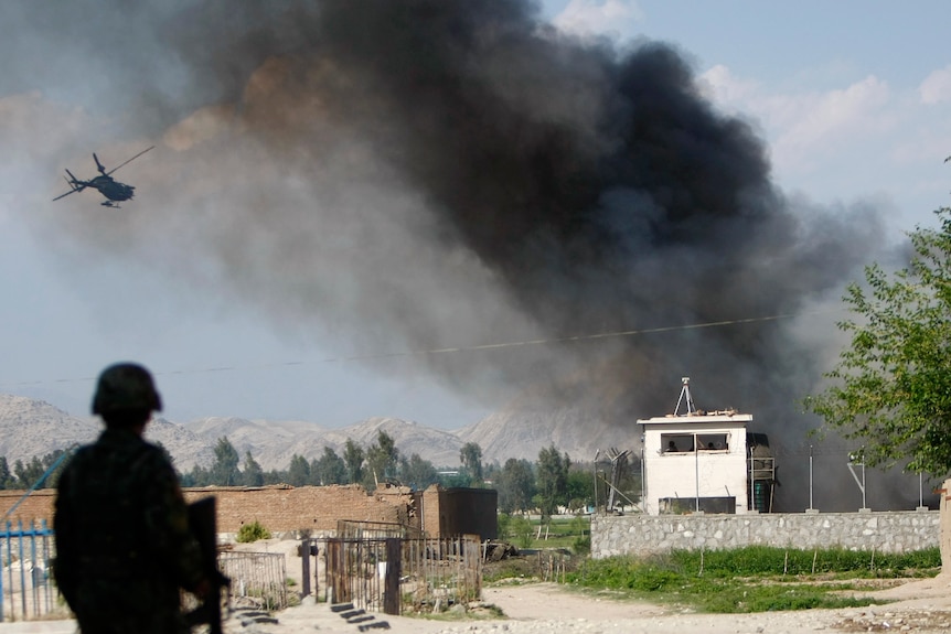 An Afghan soldier keeps watch as a NATO helicopter surveys the site of an attack in Jalalabad province.