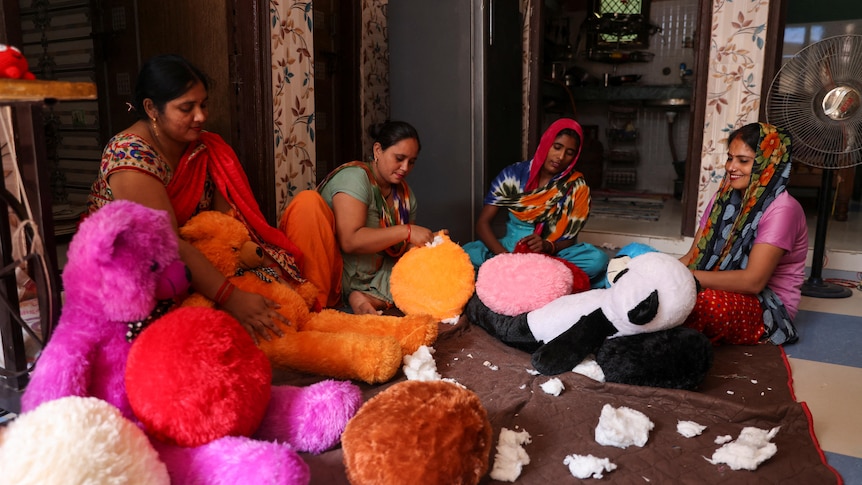 Sitting on the floor, four women work on making bright soft toys, including a panda. 