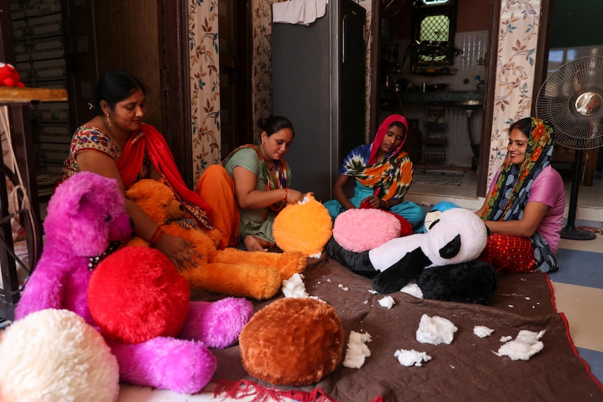 Sitting on the floor, four women work on making bright soft toys, including a panda. 